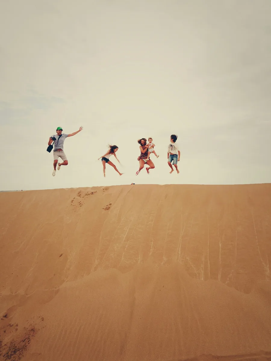 A family leaping together along the crest of a sunlit sand dune