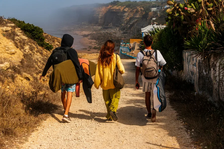 Three friends carrying surfboards down a coastal path at golden hour